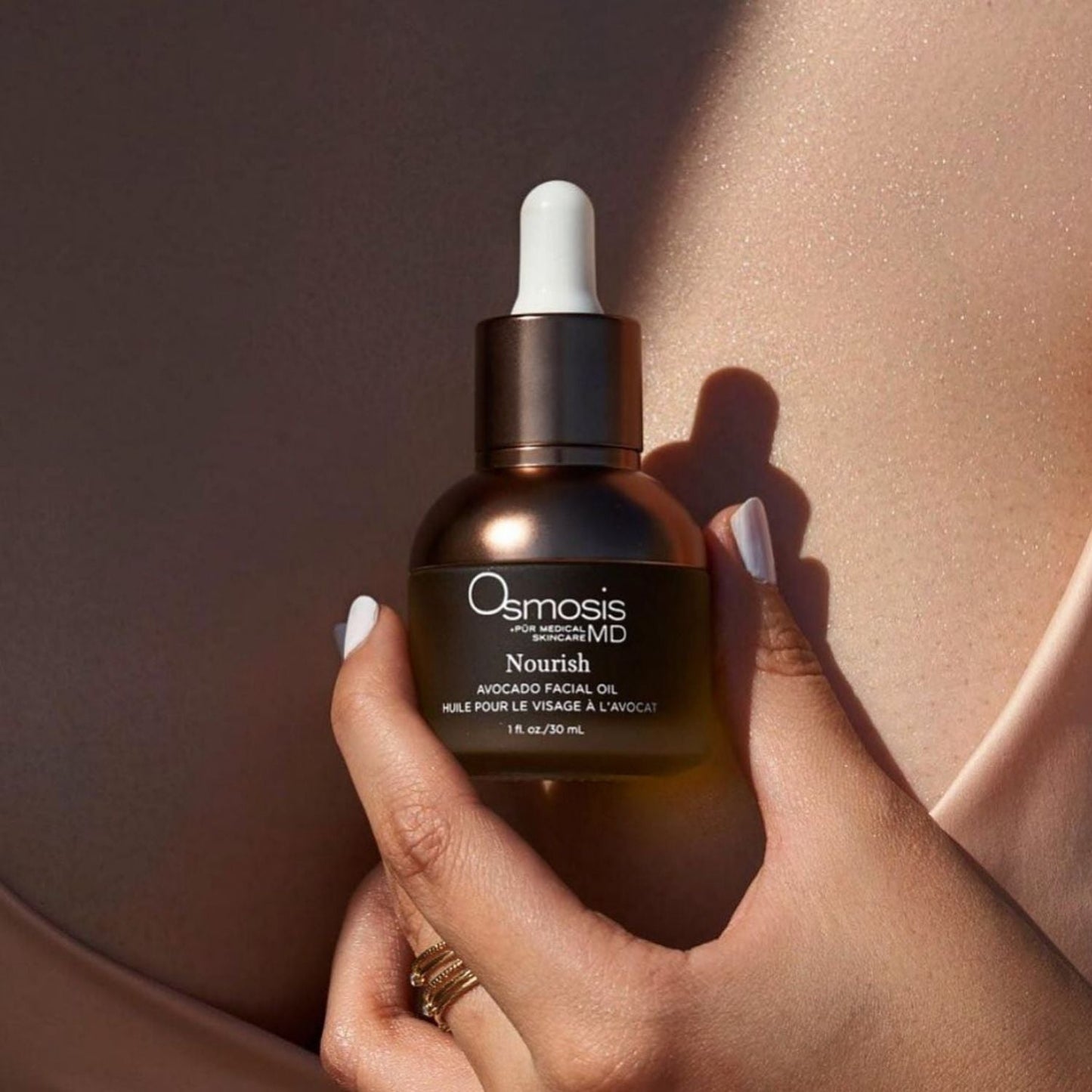 model holding a bottle of nourish oil in her hand in front of her chest