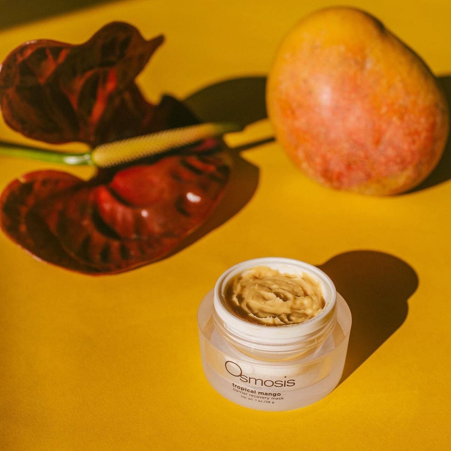 osmosis tropical mango enzyme exfoliant jar opened and displayed next to a mango