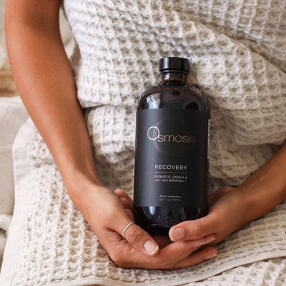 model holding a bottle of recovery by osmosis while she is wrapped in a towel